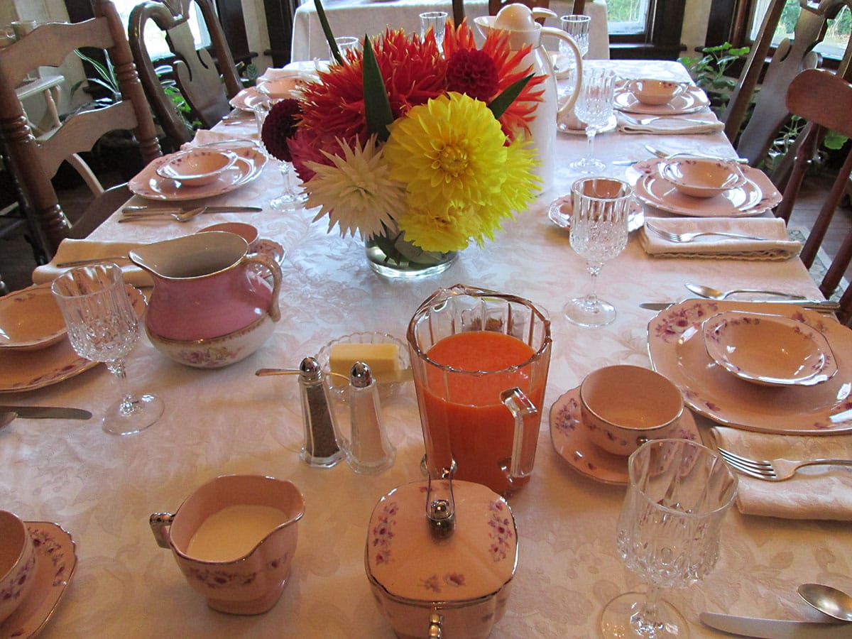 Dining room table setting with china, a bowl of fruit, and baked goods