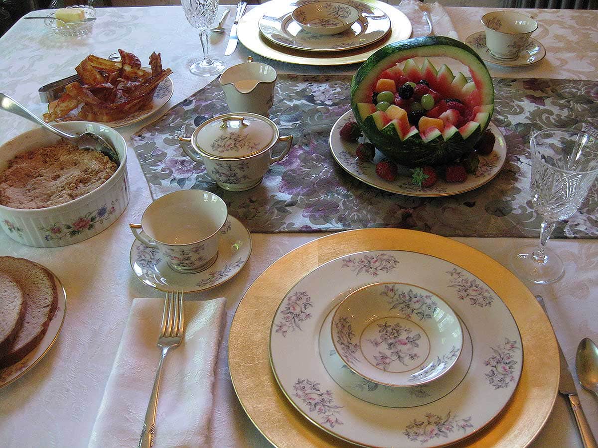 Dining room table setting with carved watermelon basket full of fresh fruit and other food