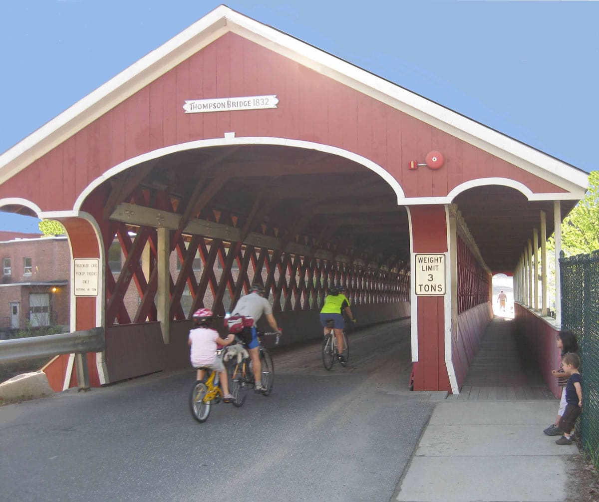 Bicyclists ridng through Thompson Covered Bridge Thompson Covered Bridge with bicyclists riding through and two little children on the side watching